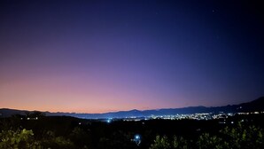 Un paisaje urbano nocturno con un cielo degradado que va del morado al azul, y luces de la ciudad a lo lejos.