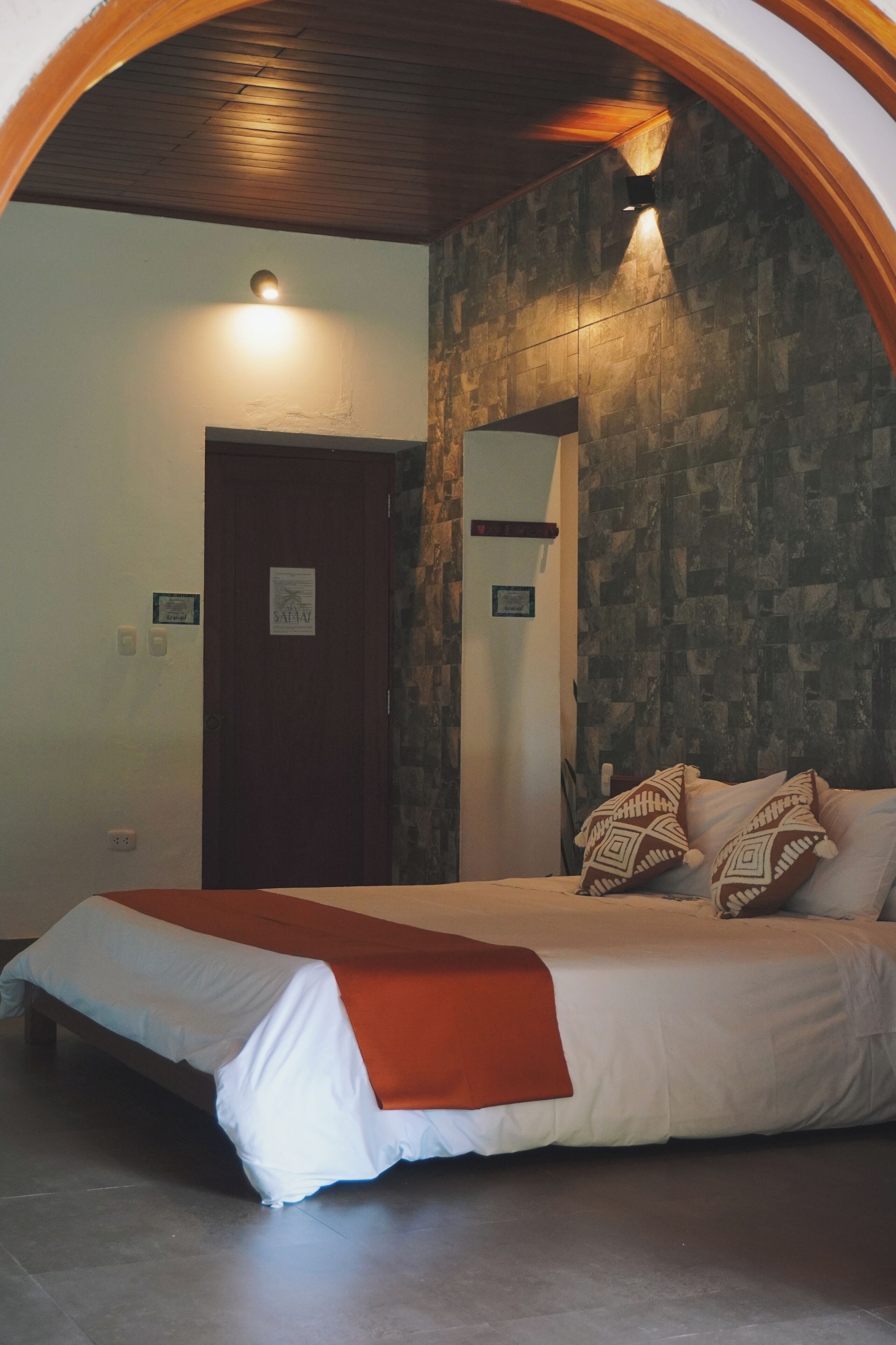 Un dormitorio con una cama, techo de madera, pared de piedra y una puerta.