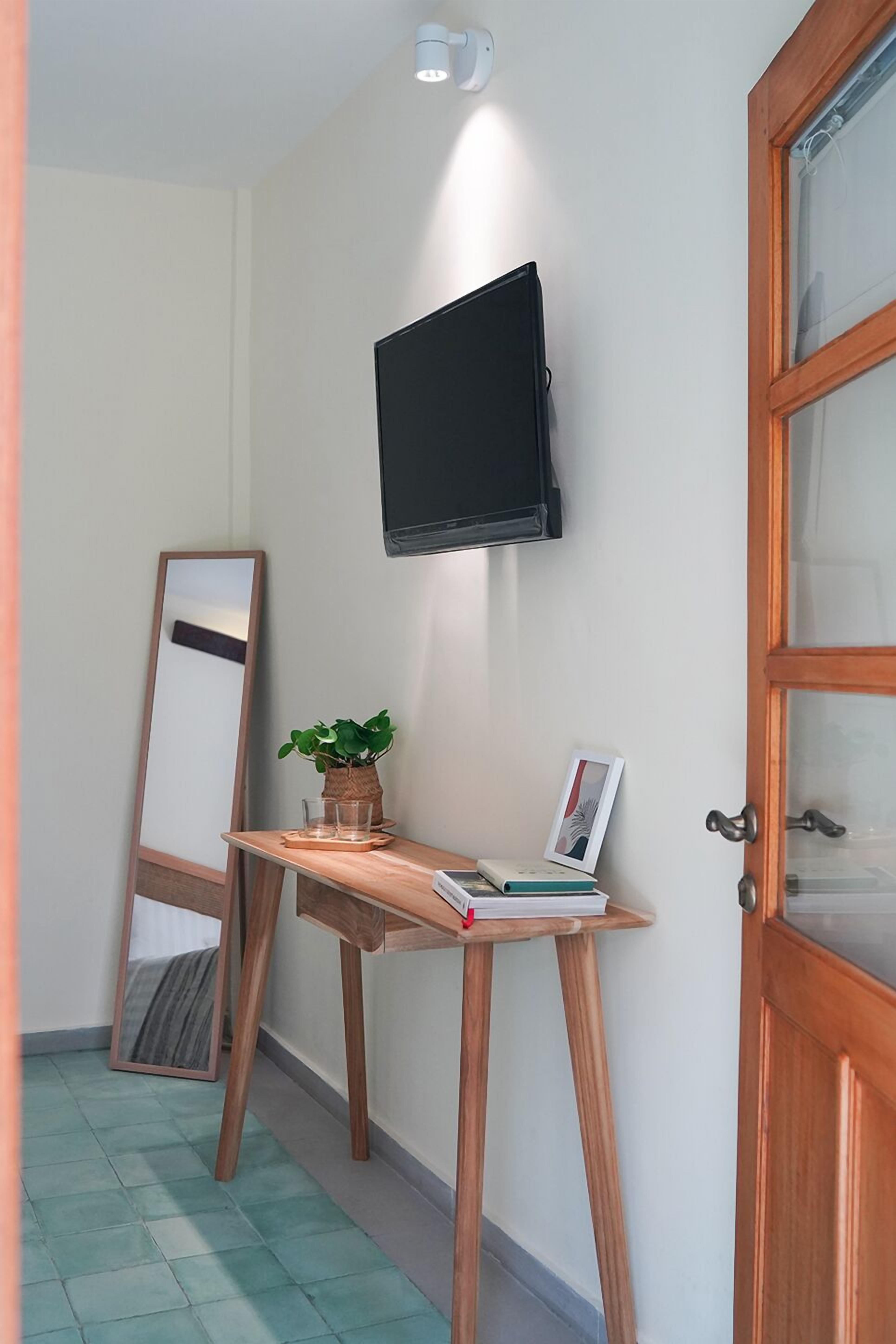 A room with a wooden desk, a flat-screen TV mounted on the wall, a large mirror leaning against the wall, and a wooden door with glass panels.