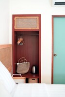 Un armario de madera con parte superior trenzada, una barra para colgar ropa y un estante con una bolsa y una tetera.