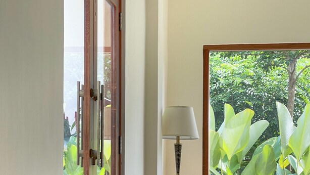 Una stanza con mobili in vimini, una lampada e vista su del verde all'esterno.