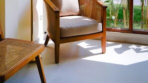Una stanza con un'ampia finestra, una sedia di legno, una lampada da terra e vista su del verde all'esterno.