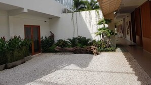 Un edificio moderno con una tettoia, un cortile in ghiaia e diverse piante.