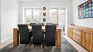 A modern dining area with a wooden table and black chairs, large windows, and a colorful abstract painting on the wall. - Apartment - Sleeps 4 - Harbour Views - Parking (Aalborg)