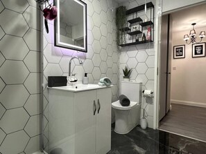 Ein modernes Badezimmer mit einem Rückwandpaneel aus sechseckigen Fliesen, einem weißen Waschtisch mit Spiegel, einer Toilette und einer Duschkabine.