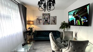 A modern living room with a glass coffee table, two armchairs, a sofa, a chandelier, and a flat-screen TV. - Remarkable 2-Bed Apartment in Castlebar (Castlebar)