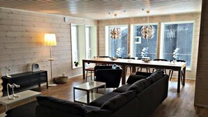 A modern living room with a black sofa, a dining table, and a chandelier.