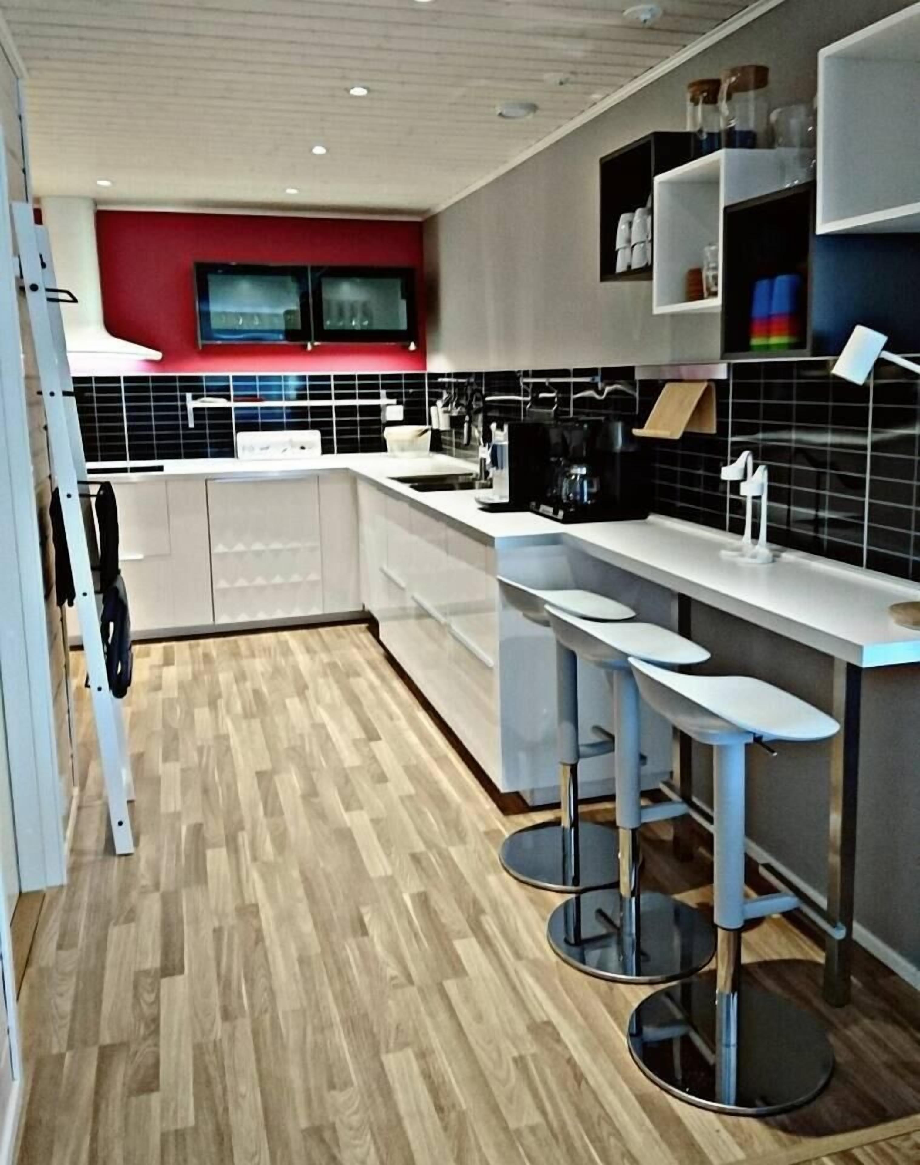 A modern kitchen with a central island, bar stools, and a red accent wall.