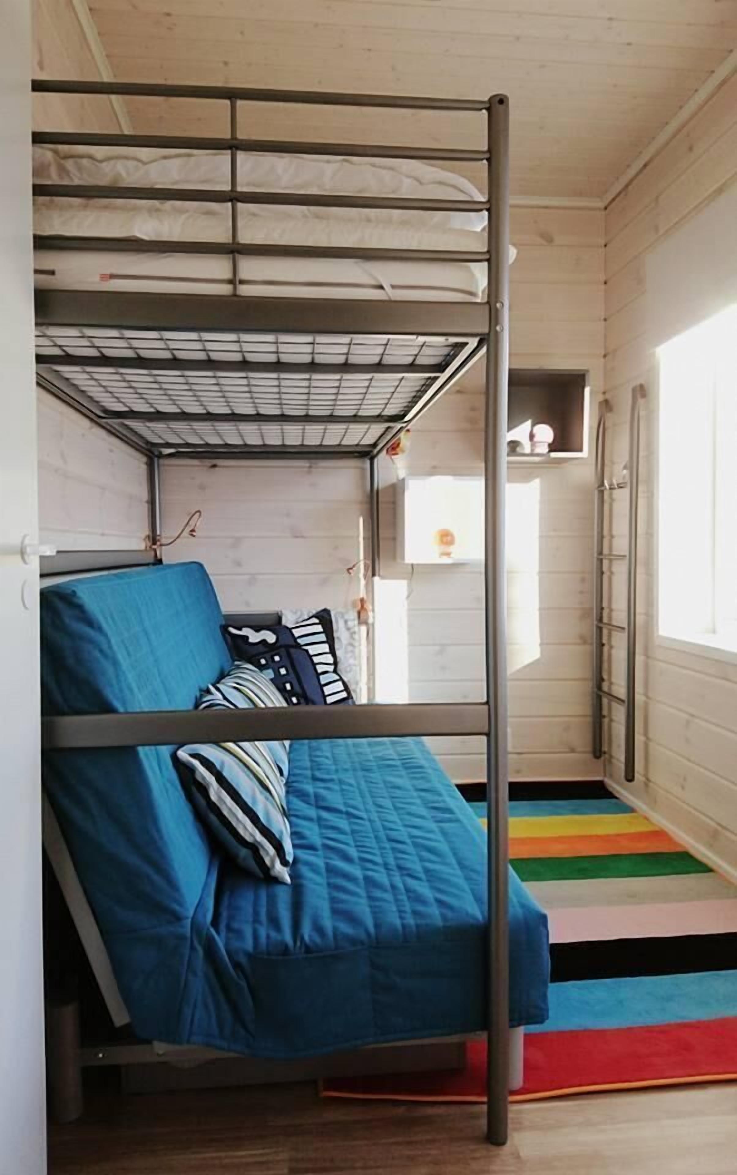 Een stapelbed met een metalen frame, blauw beddengoed en een kleurrijke gestreepte vloerkleden.