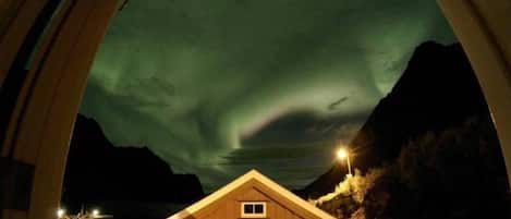 A wooden cabin with a sign reading "SANDO BLU" under a night sky with the aurora borealis.