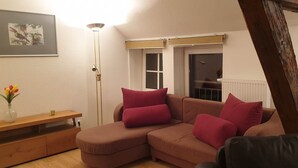 Un salon chaleureux avec un canapé d’angle marron, une petite table d’appoint en bois, un lampadaire et un tableau encadré accroché au mur.