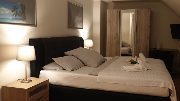 Une chambre à coucher bien rangée, avec un lit, des lampes de chevet, un miroir et un téléviseur.