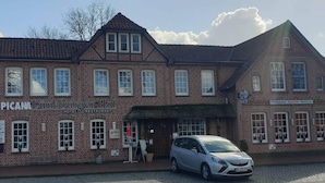 Un bâtiment en briques avec une enseigne indiquant « PICAMAH Lüneburger Hof Hotel & Restaurant » et une voiture garée devant.