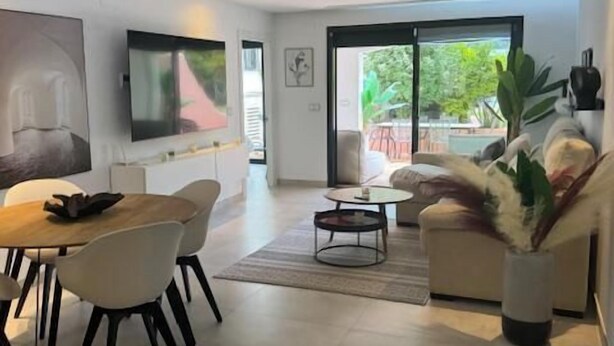 Una sala de estar moderna con comedor, televisor de pantalla plana en la pared y un ventanal con vistas al exterior.