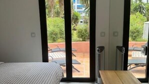 Un dormitorio con cama, una mesita pequeña y un ventanal corredero que da a un patio al aire libre.
