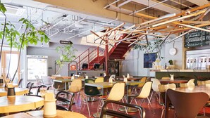 A modern cafe with multiple seating areas, a craft beer refrigerator, and a staircase leading to an upper level. - WPÜ HOTEL SHINJUKU (Tokyo)