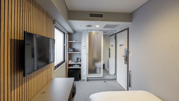 A hotel room with a flat-screen TV mounted on a wooden wall, a bed, a desk, and a walk-in closet. - WPÜ HOTEL SHINJUKU (Tokyo)