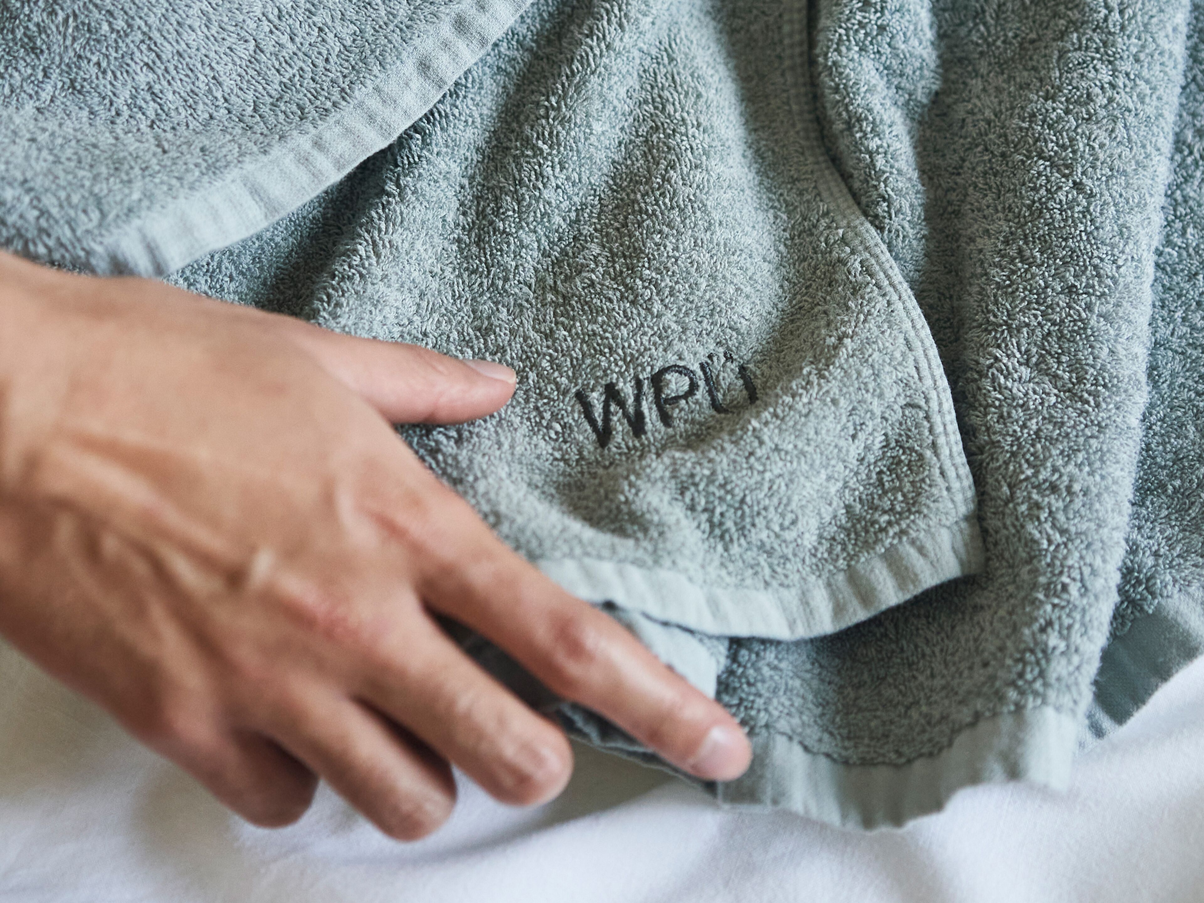 A hand touching a textured, grey towel with the letters "WPL" embroidered on it.