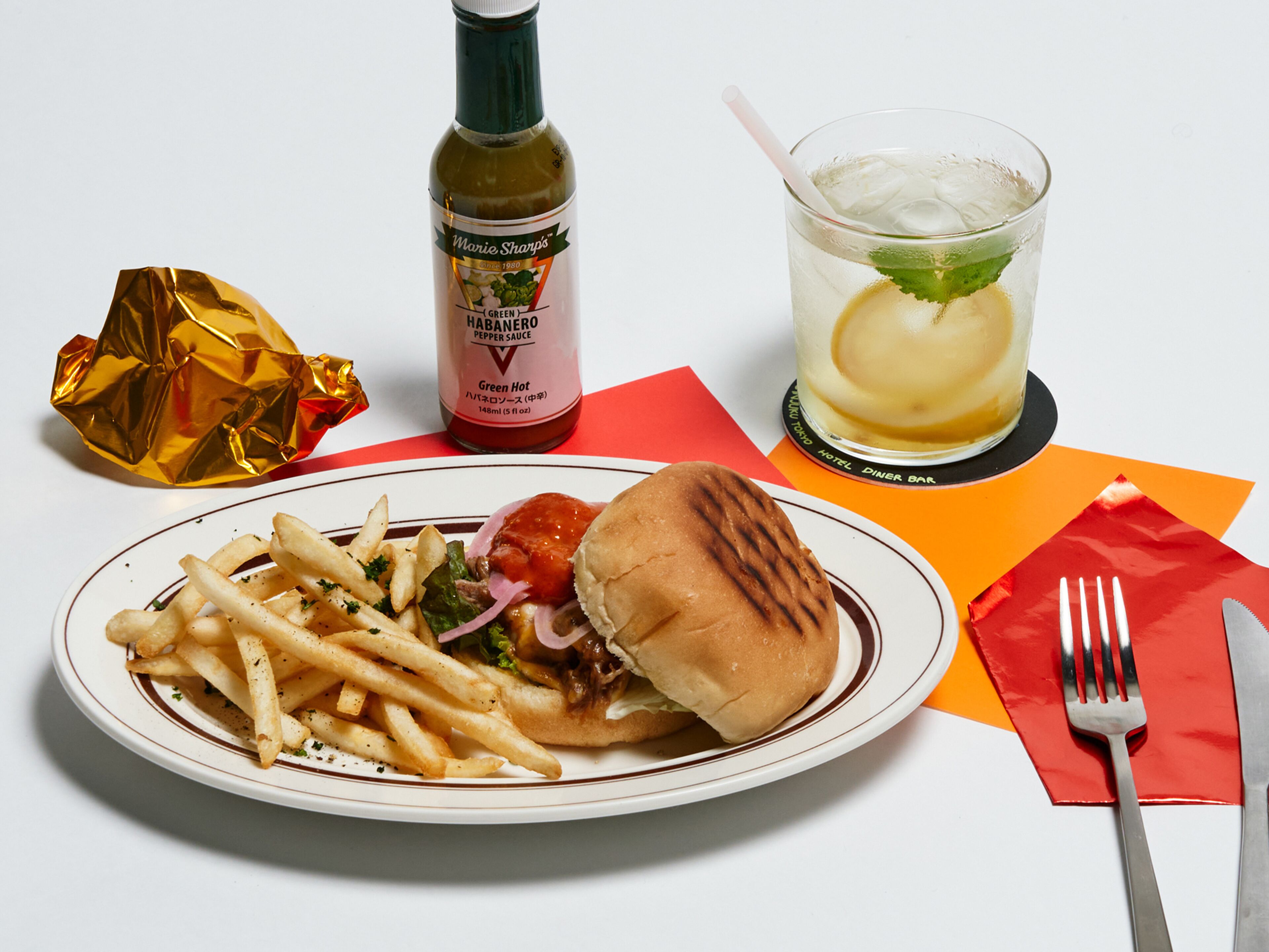 Un plato con un sándwich, papas fritas y una botella de salsa.