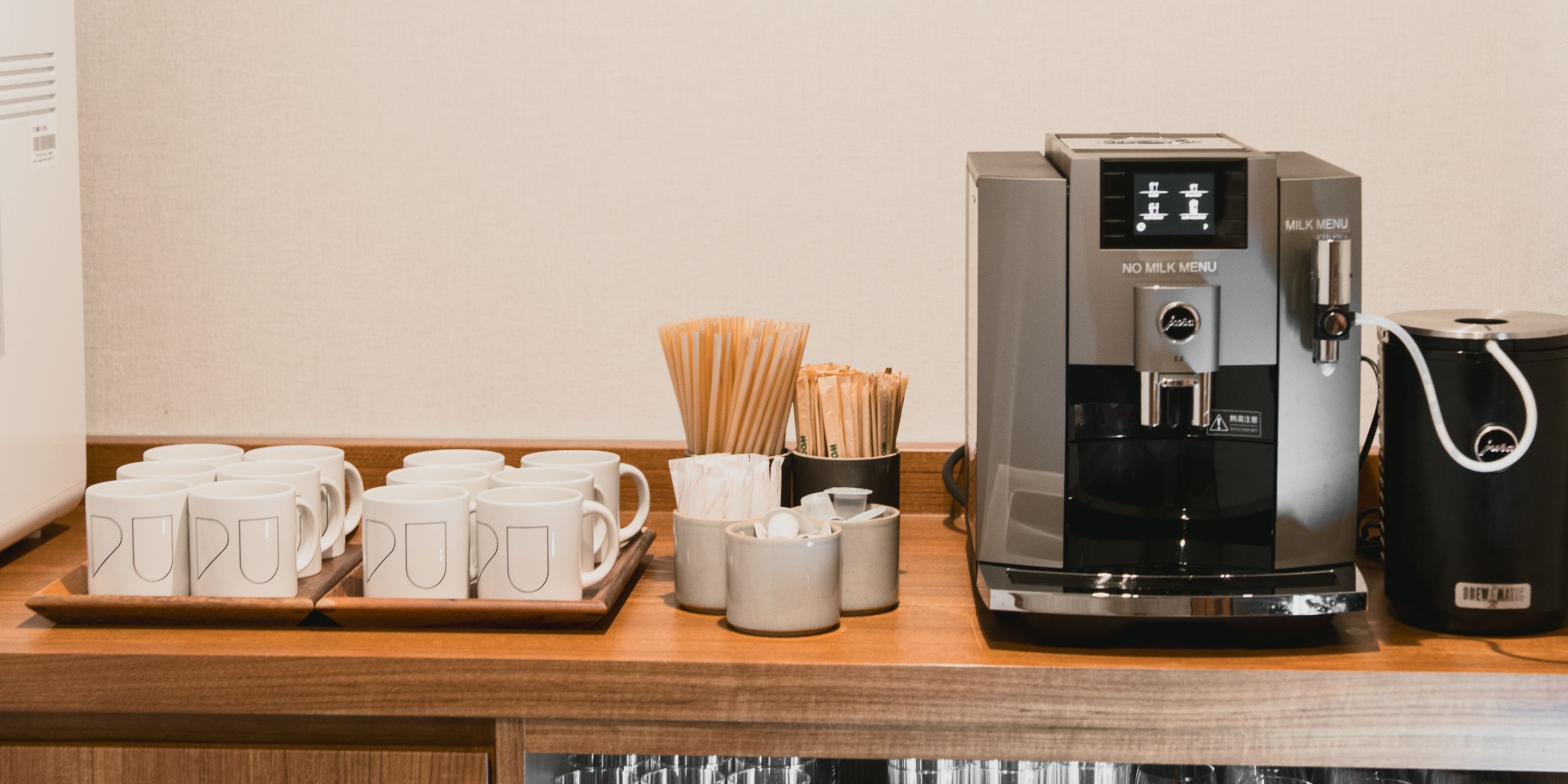 A coffee station with a coffee machine, disposable cups, and a tray of coffee cups.