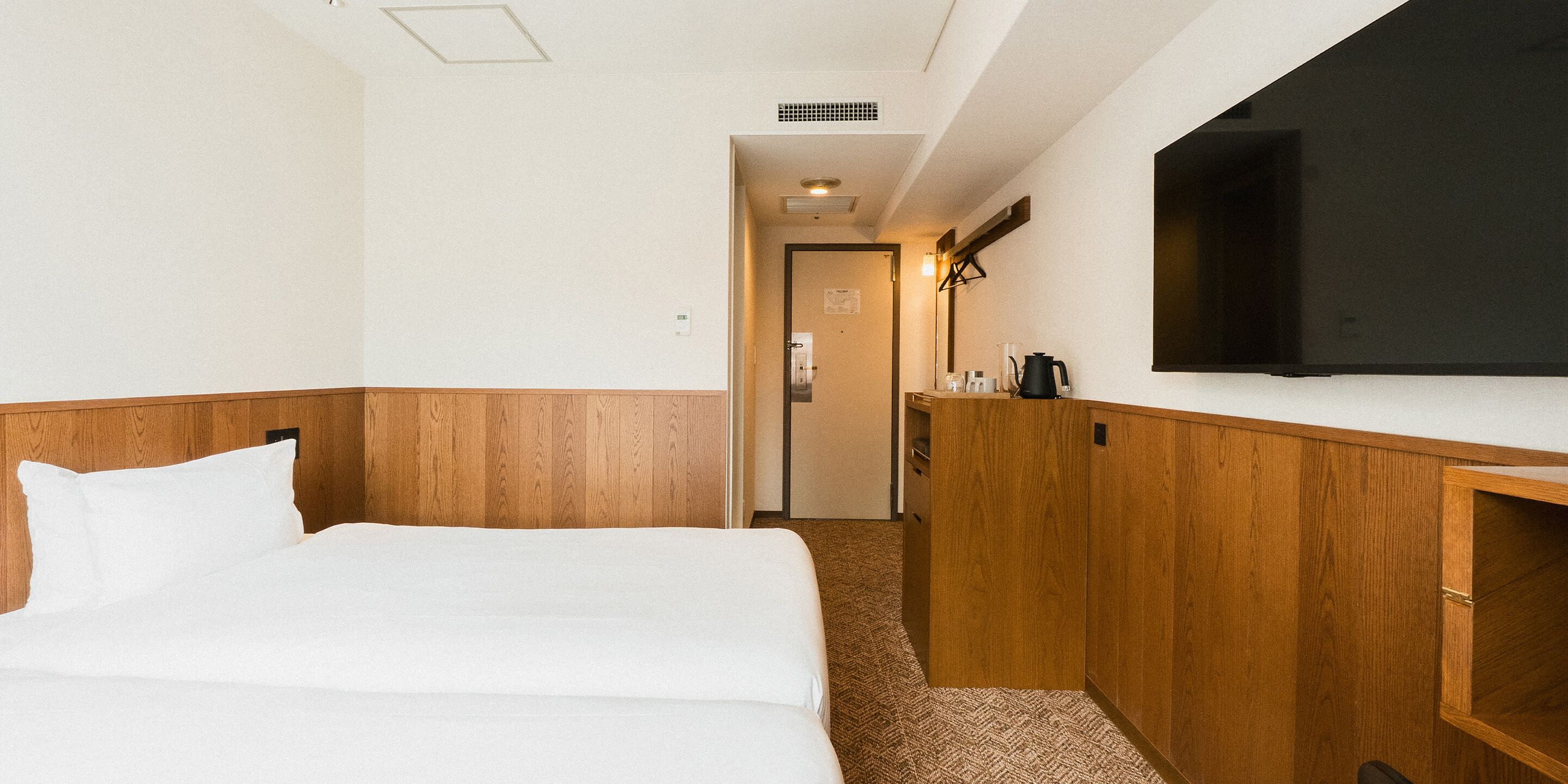 Una habitación de hotel con una cama, un televisor, un armario de madera y una puerta que da a otra habitación.
