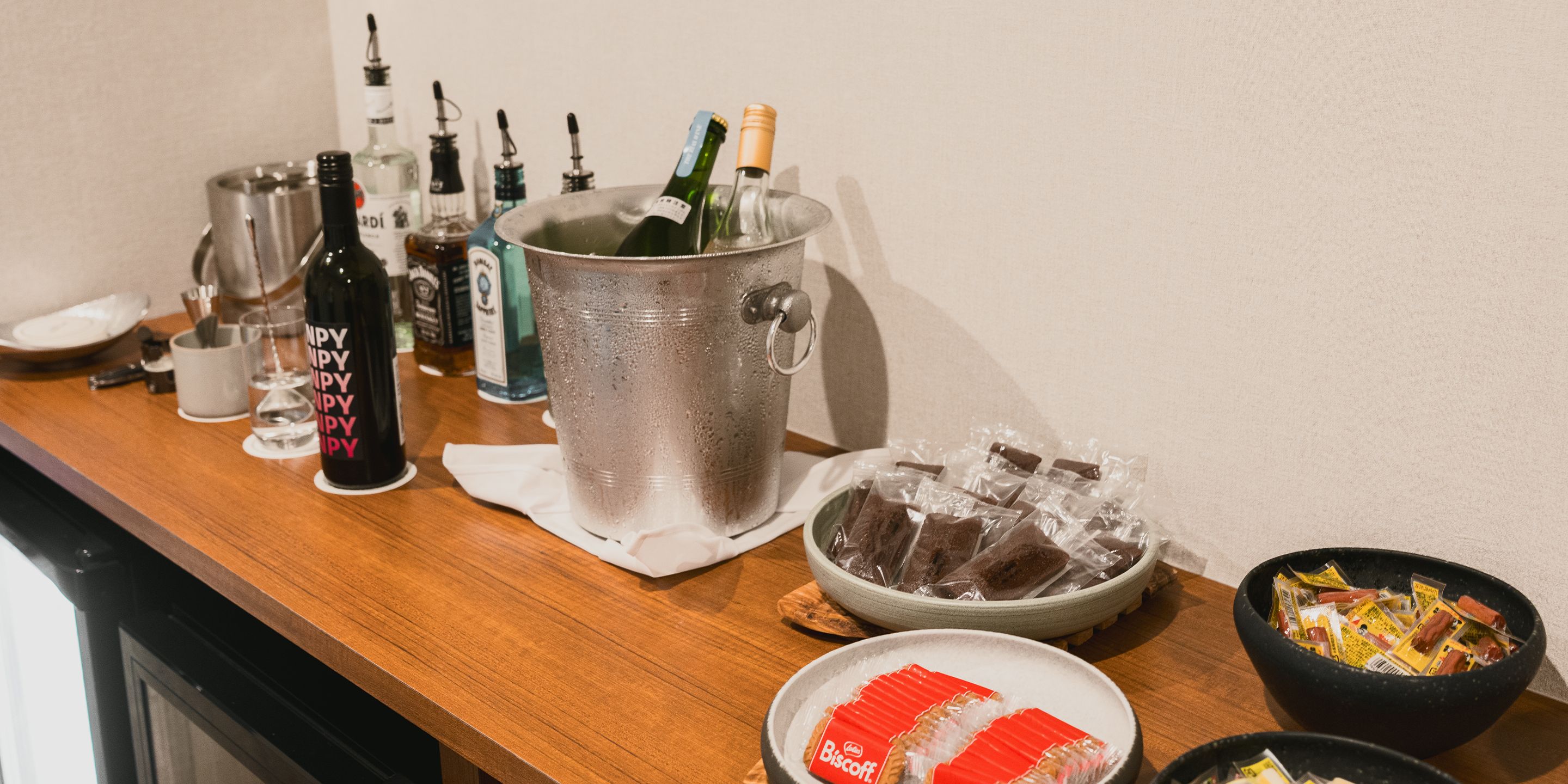 Una zona de bar con una variedad de botellas, un hielero grande y cuencos con aperitivos.