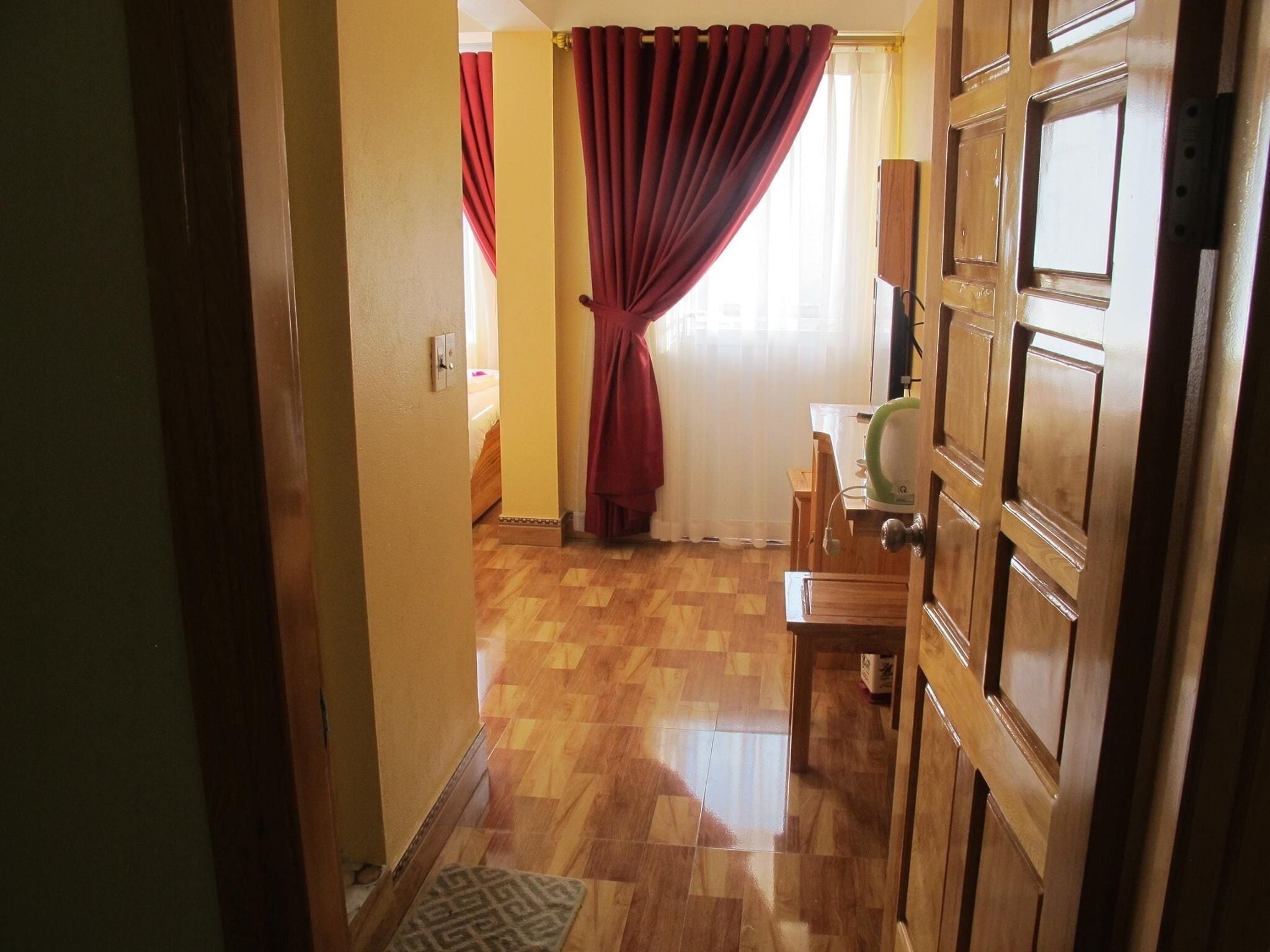 A hallway with wooden flooring, a door with a brass handle, and a window with red curtains.