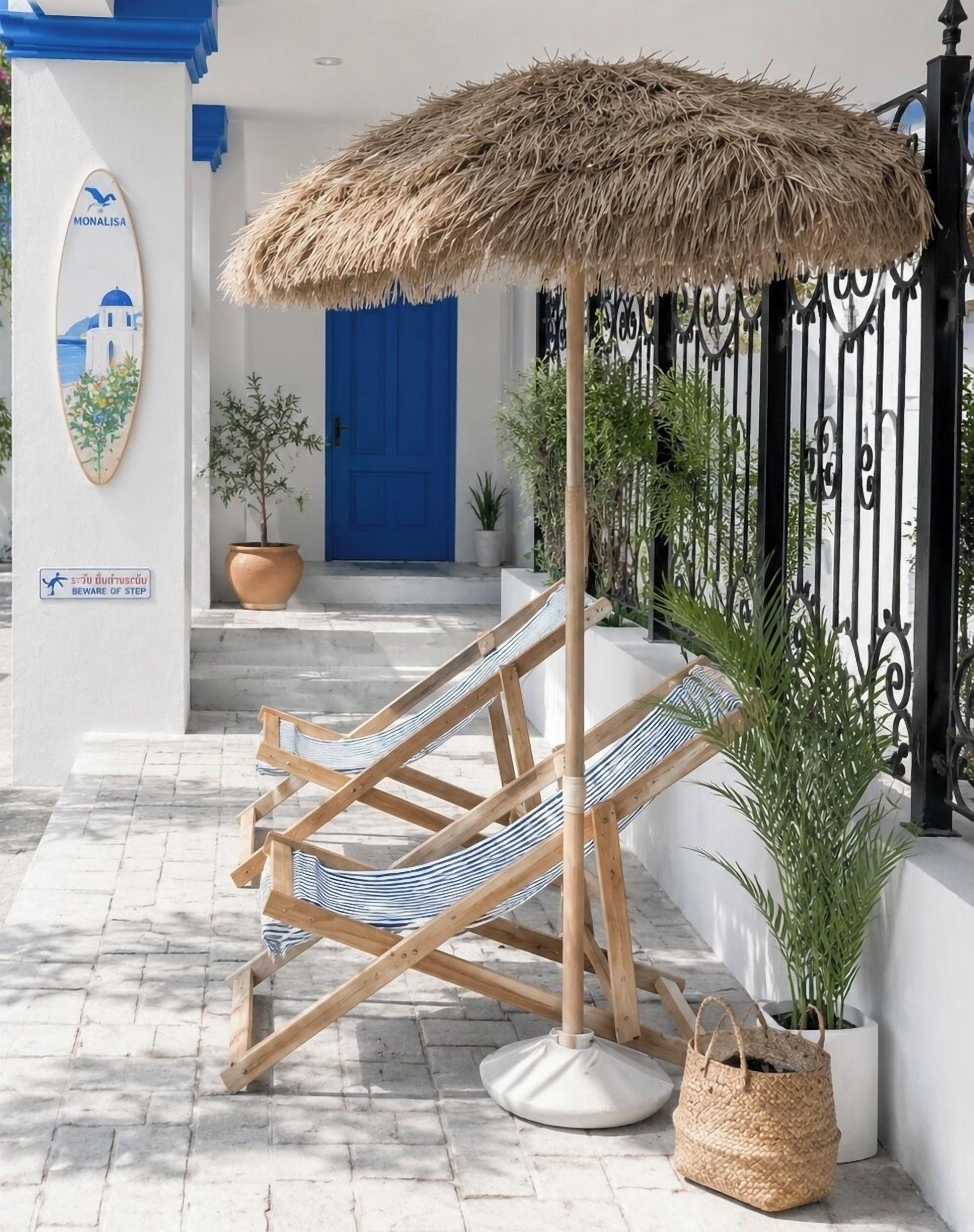 Una silla de playa bajo un toldo de paja, una puerta azul y un cartel de advertencia en la pared.