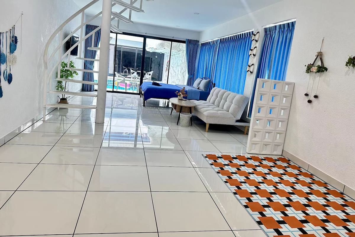 Ein modernes Hotelzimmer mit großem Balkon, einer Couch, einem Esstisch und einem gemusterten Teppich.