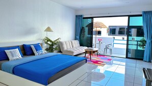 Una habitación de hotel moderna con una cama grande, un sofá, una mesita y un balcón con vistas.