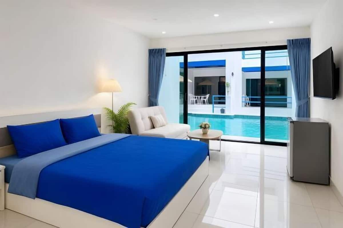 Ein Hotelzimmer mit Bett, Sofa, kleinem Tisch, Fernseher und Blick auf einen Swimmingpool.