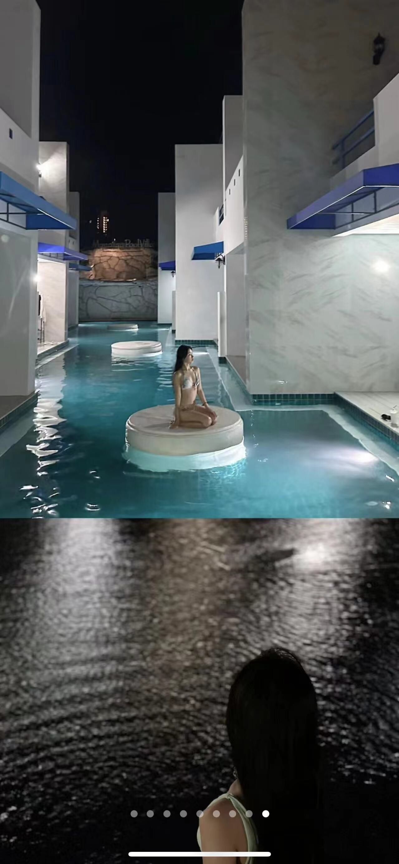 A woman sitting on a floating platform in a pool area with modern architecture and a stone wall in the background.