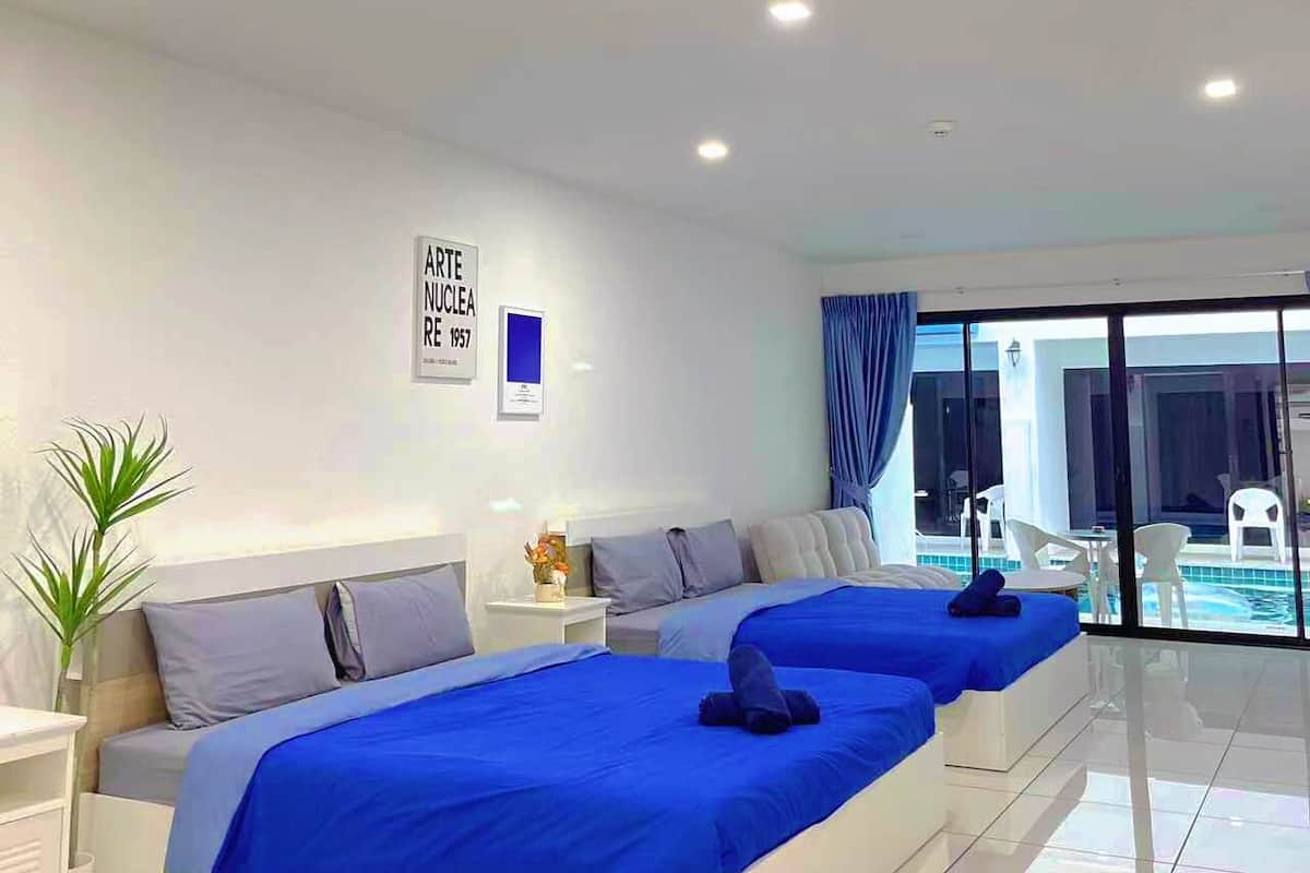 Ein modernes Hotelzimmer mit einem großen Bett, einem kleinen Nachttisch, einer Topfpflanze und Blick auf den Pool.
