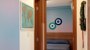 Un couloir étroit mène à une chambre à coucher où se trouvent un lit, une carte du monde et des œuvres d’art murales abstraites.