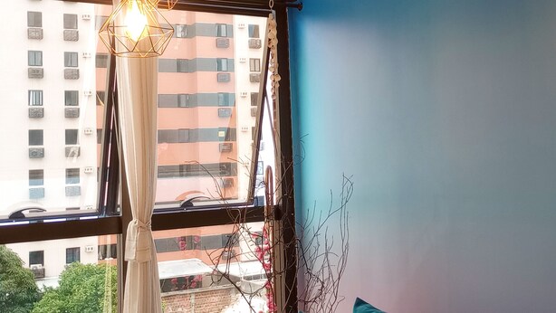 Une pièce avec un mur bleu, une fenêtre avec des rideaux, un canapé bleu et un luminaire suspendu.