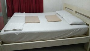 Uma cama de solteiro com colchão branco e almofadas bege, cortina vermelha e parede lisa.