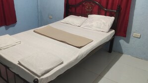 Uma cama bem arrumada com roupas de cama brancas e bege, uma cabeceira de metal e cortinas vermelhas.