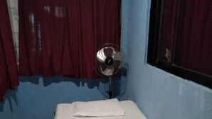 Quarto pequeno com uma cama de solteiro, estrutura de madeira, colchão branco e cortina vermelha.
