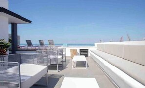Eine Dachterrasse mit Sitzgelegenheiten im Freien, einem weißen Tisch und Blick aufs Meer.