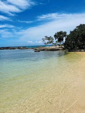 A beach with clear shallow water, rocky outcrops, and dense foliage. -  Charming 3-bedroom house with large backyard , WiFi Lucea. Access  pool and Gym (Lucea)