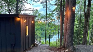 A cabin with a gravel path leading to a wooden deck, surrounded by trees and a lake. - Waterfront ADK Cabin and 2 Micro-cabins (Corinth)