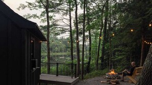 A cabin with a deck, a fire pit, and a view of the forest. - Waterfront ADK Cabin and 2 Micro-cabins (Corinth)