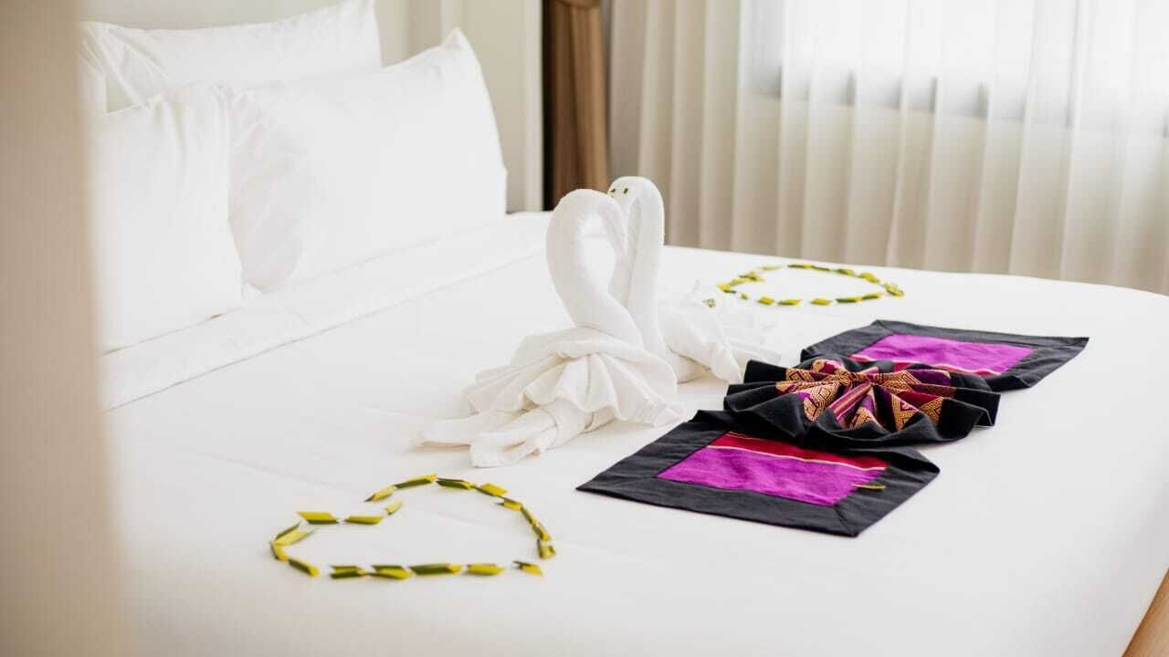 A hotel room with a neatly made bed, a towel art arrangement, and a decorative pillow.
