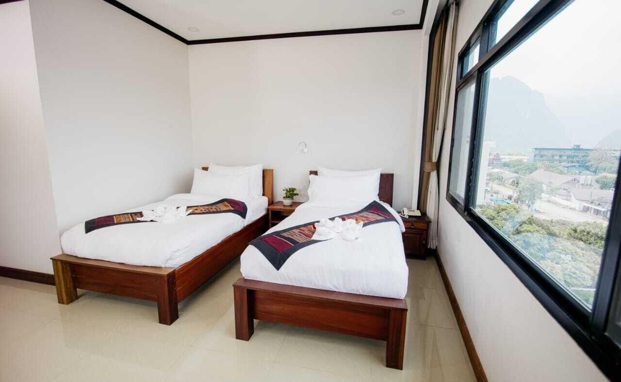 A hotel room with two wooden beds, white bedding, and a large window offering a view of a mountainous landscape.