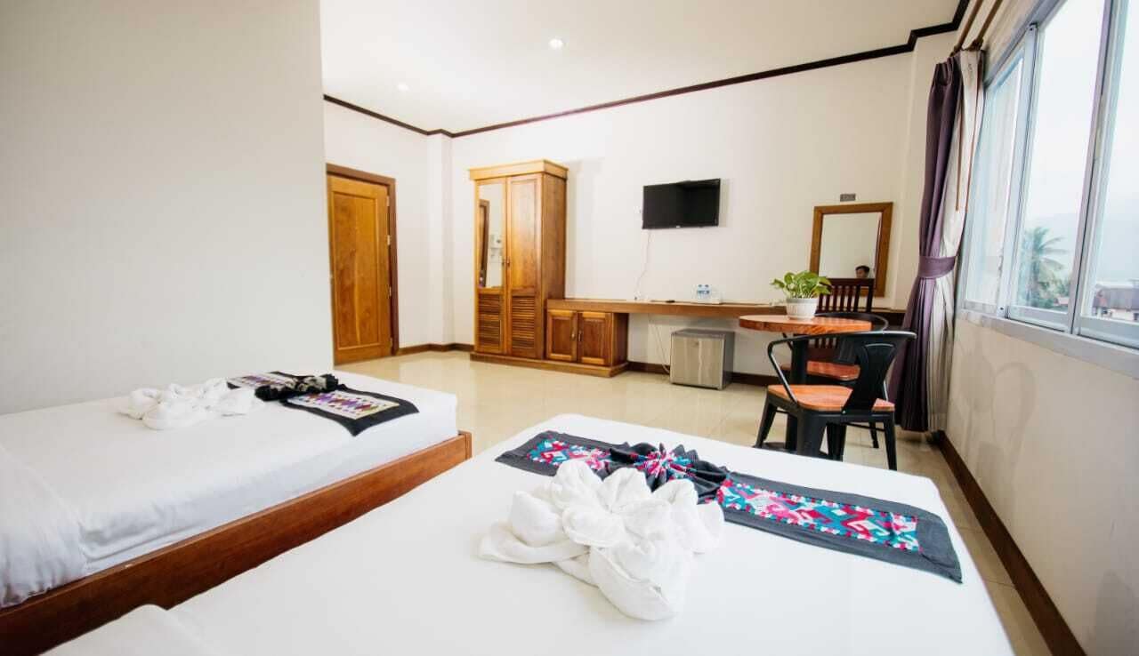 A hotel room with two beds, a desk, a chair, a TV, and a window.