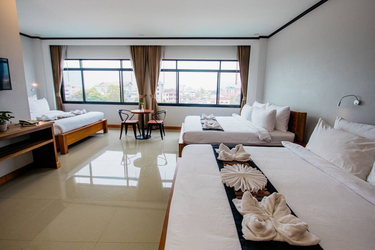 A hotel room with two beds, a desk, a chair, a TV, and a window with a view of buildings.