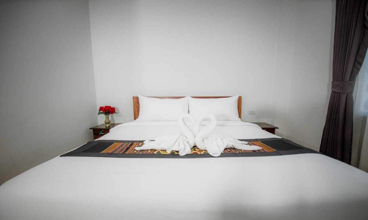 Een hotelkamer met een net opgemaakt bed, een klein nachtkastje met een bloevas en een raam met gordijnen.