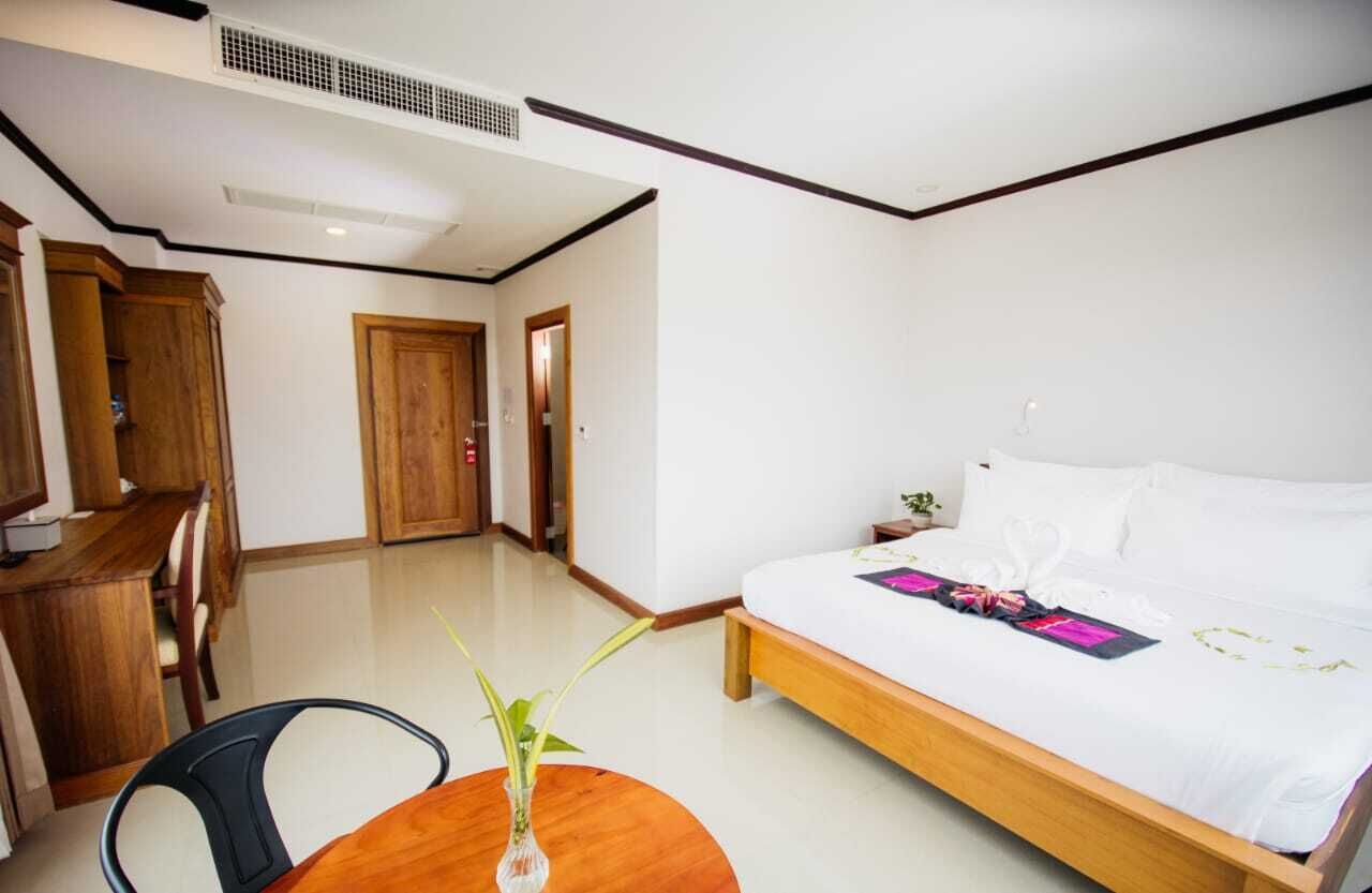 A bedroom with a bed, a wooden desk, a chair, and a small table with a vase.