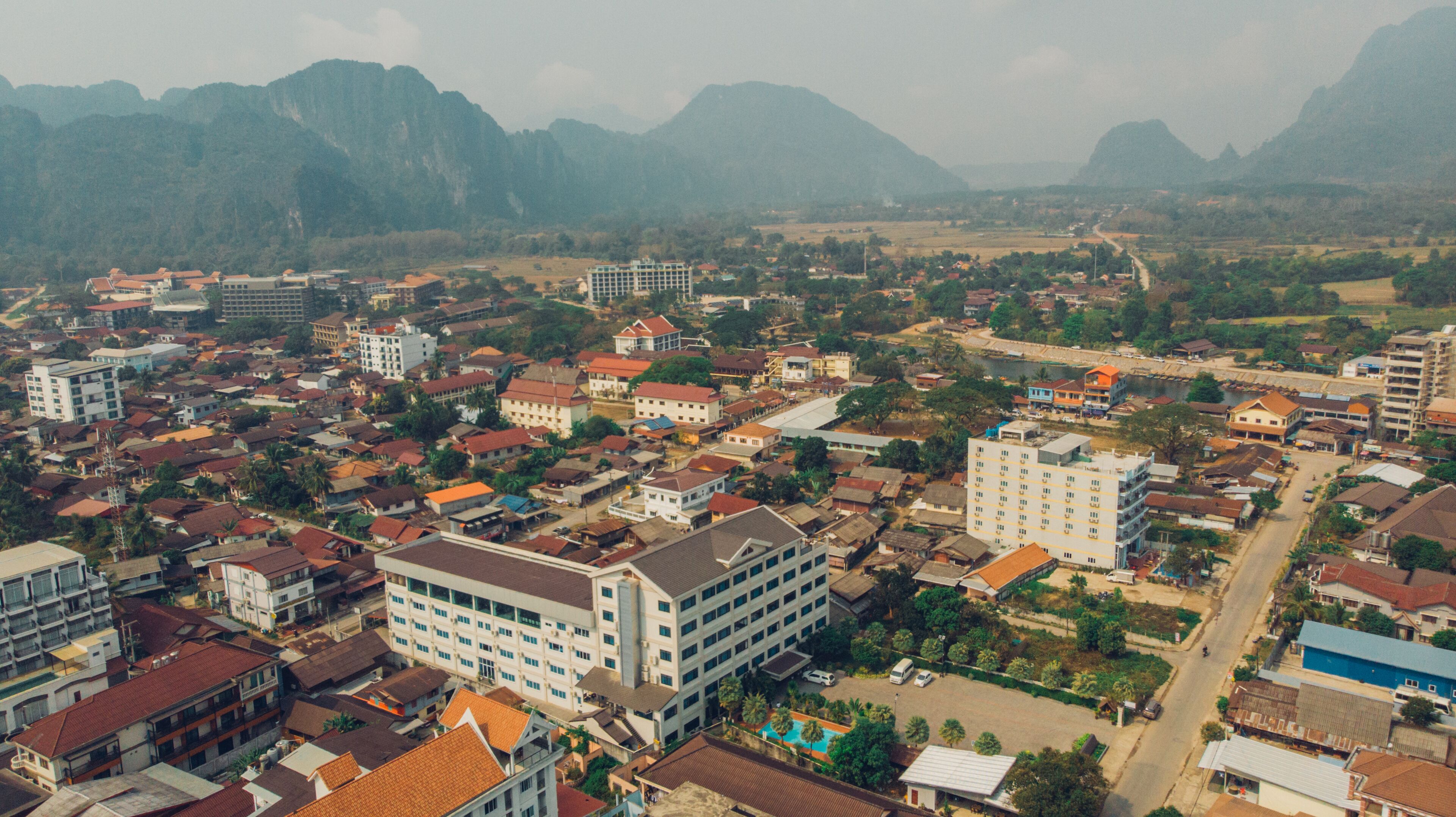 An aerial view of a town with various buildings, including a prominent hotel with multiple floors and a swimming pool.