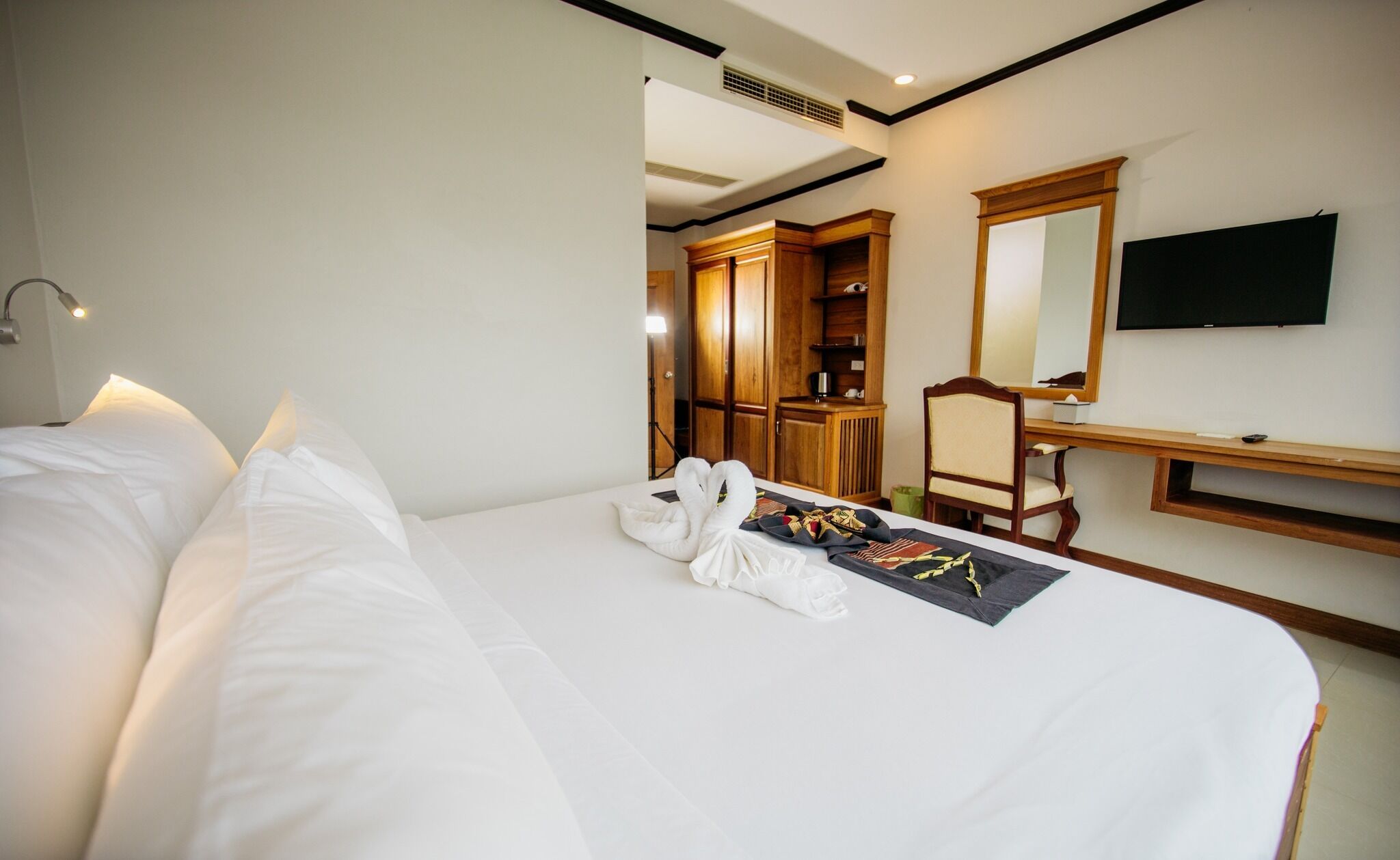 A hotel room with a large bed, a desk with a chair, a mirror, and a television.